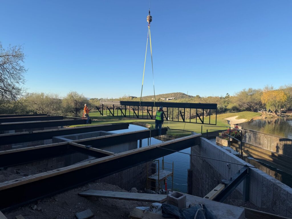 Crane setting steel bridge framing over water at a Tucson resort